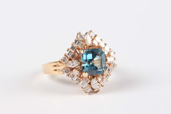 TooveysA gold, blue topaz and diamond cluster ring, claw set with the cut cornered square cut blue topaz within a surround of marquise, baguette and circular