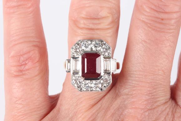 TooveysAn 18ct two colour gold, ruby and diamond cluster ring, collet set with the cut cornered rectangular step cut ruby within a surround of baguette and c