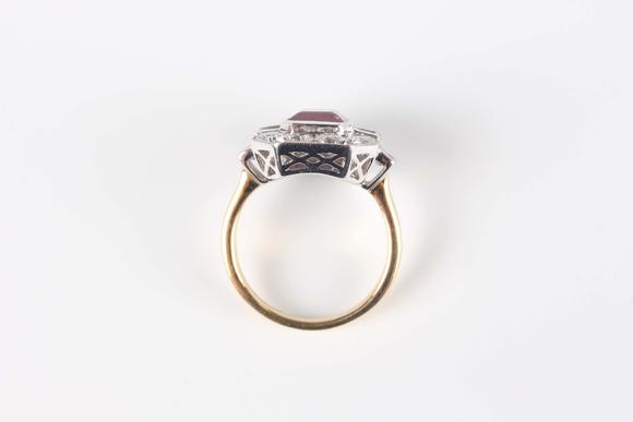 TooveysAn 18ct two colour gold, ruby and diamond cluster ring, collet set with the cut cornered rectangular step cut ruby within a surround of baguette and c