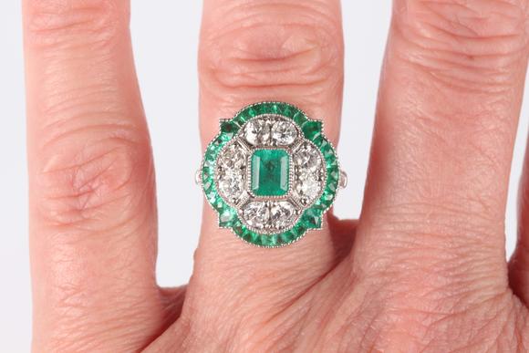 TooveysA platinum, emerald and diamond ring in an Art Deco inspired cluster design, mounted with the cut cornered rectangular step cut emerald within a quatr