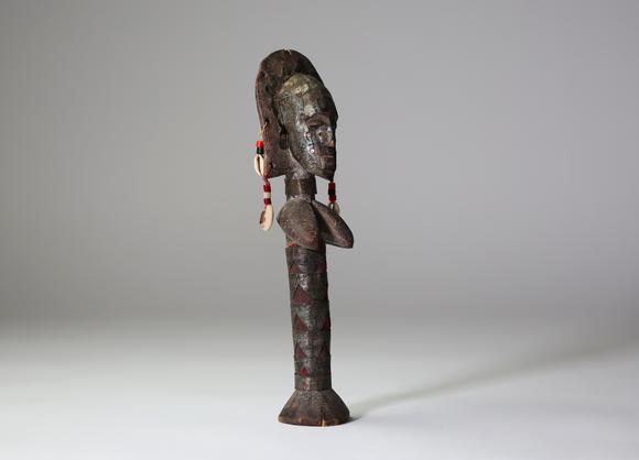 Goldfield Auction sarlsBambara / Marka, Afrique de l’Ouest.
Poupée sculptée, ornée de tissus rouges, de perles, de cauris et de 
plaques de métal gaufrées à décor de scar