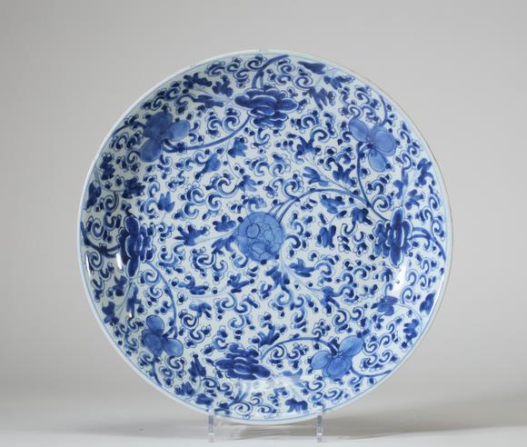 Goldfield Auction sarlsPlat en porcelaine bleu et blanc, Chine, à décor dense de rinceaux fleuris et pivoines stylisées de l’époque Kangxi, l’aile extérieure ornée de bran