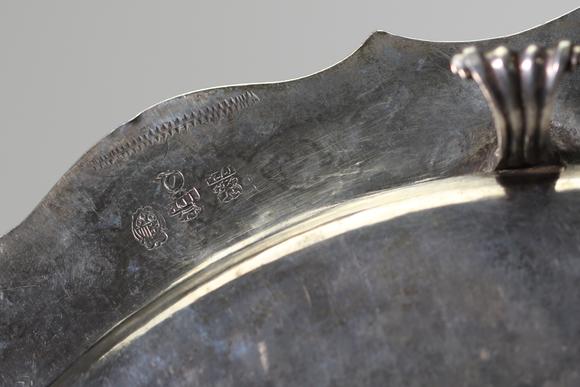 Goldfield Auction sarlsAssiette dite volante en argent massif, travail liégeois daté 1724, de forme circulaire à bord contourné et légèrement festonné. Elle repose sur trois