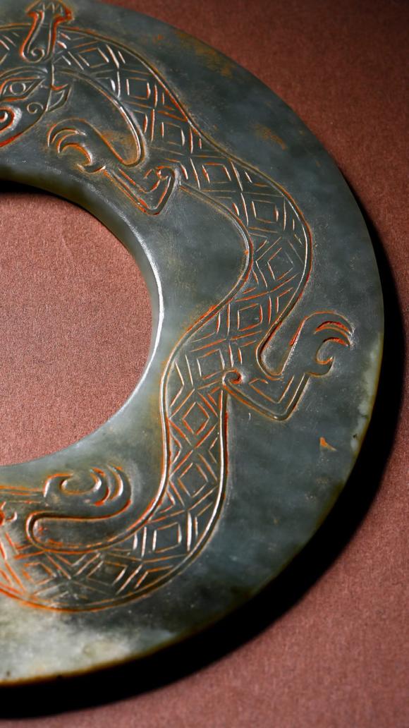 HUNG YUN ZHAI AUCTION HOUSE INCPre-Ming Dynasty Cinnabar-Infiltrated Dragon- Pattern Jade Bi Disc