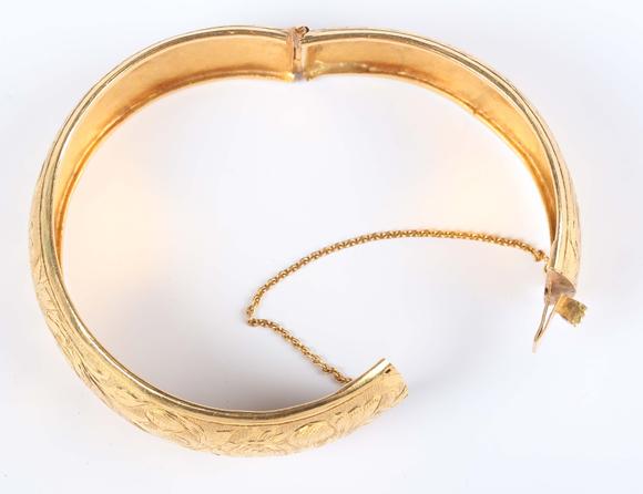 TooveysA gold circular hinged bangle with floral engraved decoration, on a