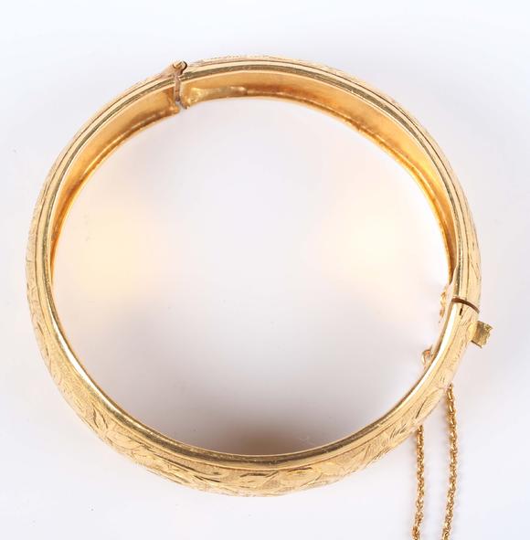 TooveysA gold circular hinged bangle with floral engraved decoration, on a