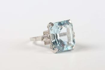 A platinum, aquamarine and diamond ring, claw set with the large cut cornered rectangular step cut aquamarine between baguette cut diamond three stone