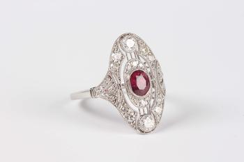 A platinum, ruby and diamond oval ring in an Art Deco inspired design, collet set with the oval cut ruby at the centre, detailed ‘Pt950’, weight 4.5