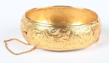 A gold circular hinged bangle with floral engraved decoration, on a