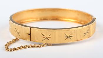A gold circular hinged bangle with facet cut decoration, detailed ‘